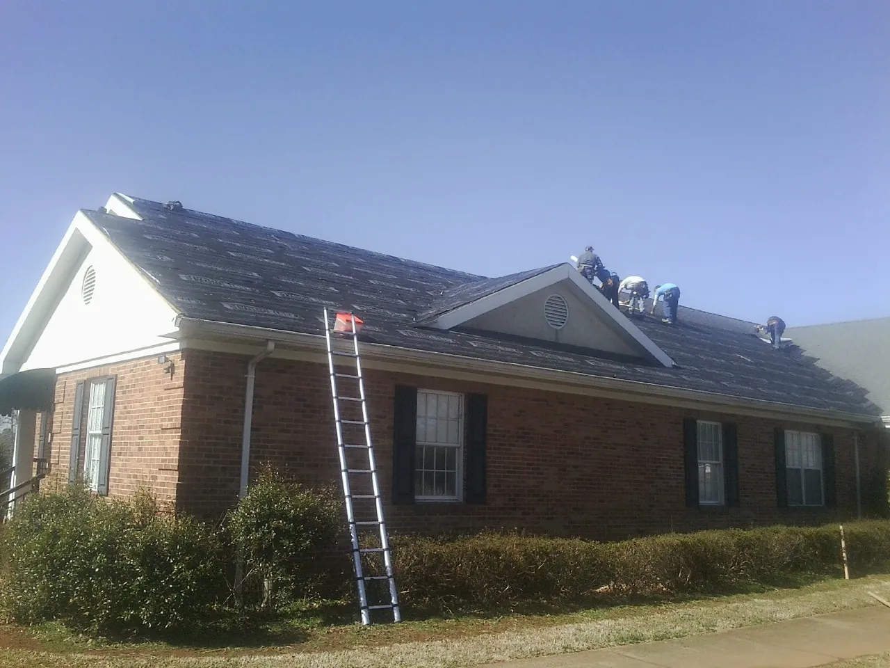 Crew tearing shingles off a brick ranch roof with a ladder set — Metal Roof Repair work by our crew in Poole