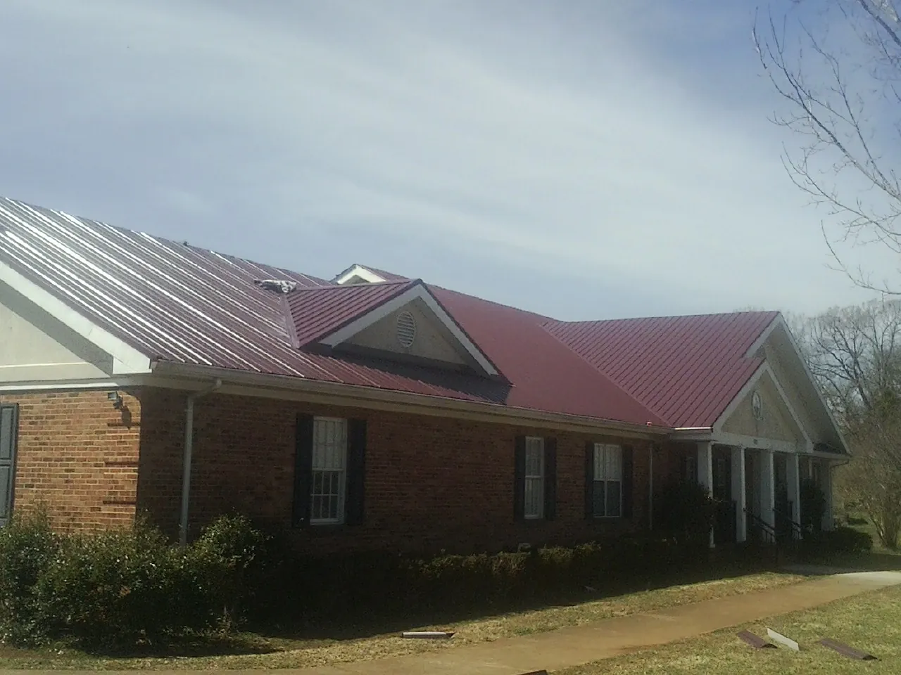 Red metal roof with gabled entries on a long brick building, from a Hail Damage Roof Repair job in Poole