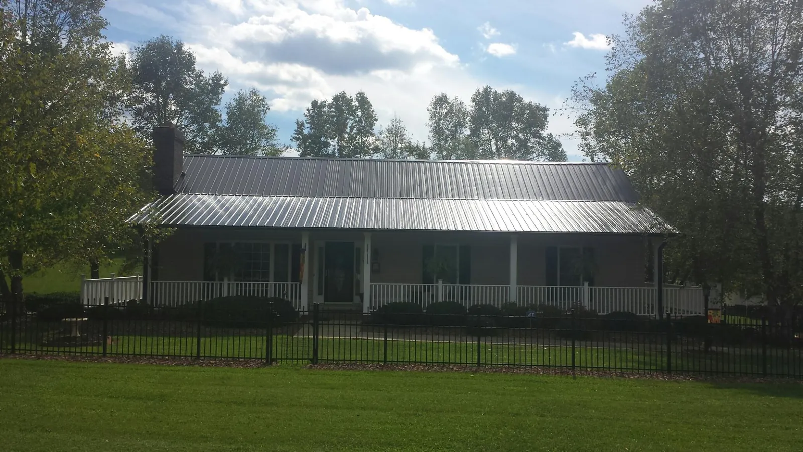 Gray metal roof on a brick ranch with a full width front porch — Gutter Guard Installation work by our crew in Poole