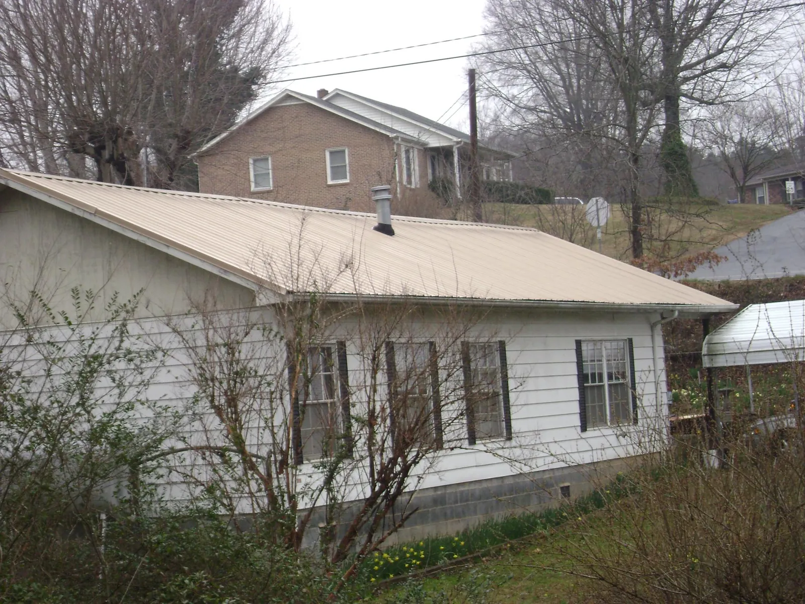 Tan metal roof on a white sided house set into a hillside — Commercial Roofing by Roofing Brothers in Poole